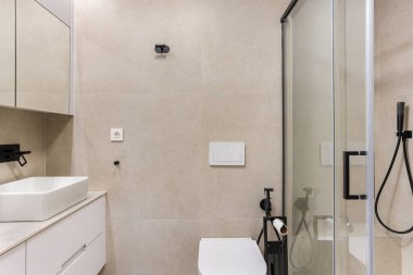 Modern banyo, cam duş, damar lavabosu, bej fayanslar ve mat siyah aksesuarlar.