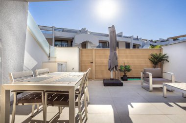 Modern teraslarda yemek alanı, şezlong, güneş şemsiyesi ve tropikal bitkiler var.