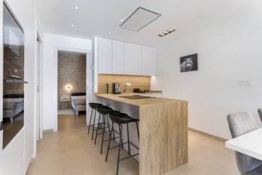 Ahşap ada, şık dolaplar, bar tabureleri ve görünür bir yatak odası olan çağdaş mutfak.