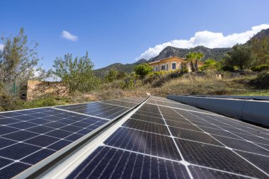 Yeryüzüne monte edilmiş güneş panelleri dağları ve mavi gökyüzü manzaralı kırsal kesimdeki villaya güç veriyor..
