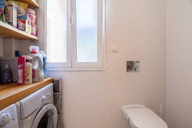 Çamaşır makinesi, deterjan deposu, pencere ve dahili tuvalet içeren kompakt kullanım alanı.