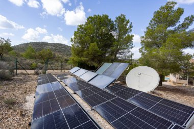 Manzaralı kırsal bir ortamda zemin üzerine kurulmuş güneş panelleri ve uydu anteni