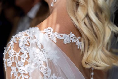 Zarif omuz danteli ve yumuşak düğün ışıklarında yakalanan dalgalı sarı bukleler.