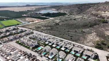 Arka planda Torrevieja Gölü ve golf tesisi olan modern evlerin üzerinde dönen insansız hava aracı.