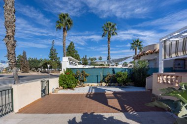 Döşeme kaplı palmiye ağaçları ve açık mavi gökyüzü olan parlak konutlu bir avlu.