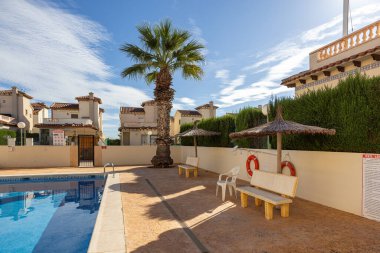 Palmiye ağaçları, şemsiyeler ve Akdeniz evleri olan açık havuz.