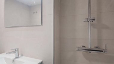 Modern minimalist banyo, krom armatürler ve aydınlık duvarlı büyük ayna.