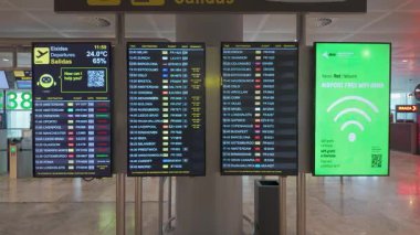 Uçuş bilgileri, yoğun havaalanı terminalinde Wi-Fi işaretli çıkış saatlerini ve kapıları gösteriyor.