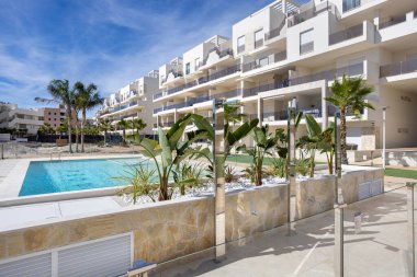 Havuz, muz ağaçları, palmiye bitkileri ve temiz beyaz mimari içeren şık konut kompleksi