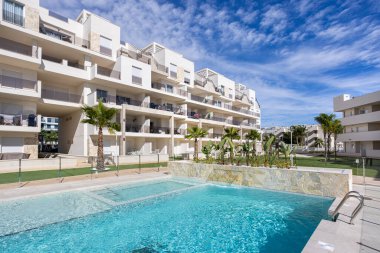 Havuz, palmiye ağaçları ve açık mavi gökyüzü ile güneşli havanın yer aldığı çağdaş konut kompleksi