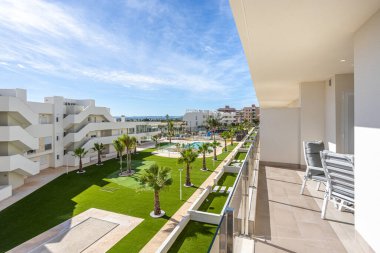 Güneşli balkon palmiye ağaçları, manikürlü çimenler ve köpüklü açık havuz.