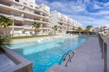 Modern residential area featuring a sunlit swimming pool, loungers, and tropical landscaping