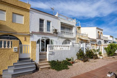 White and yellow stucco homes with balconies, tiled steps, and gravel front garden area