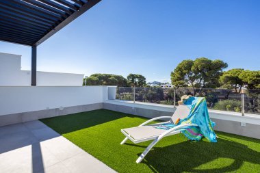 Güneşli yataklı, pergola gölgeli, suni otlu ve orman manzaralı açık çatı.