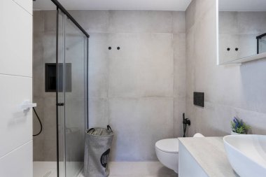 Minimalist banyo, cam duş, çamaşır sepeti ve şık modern kapaklar.