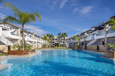 Large resort pool surrounded by palm trees and stylish white buildings at Innova Beach, Punta Prima.