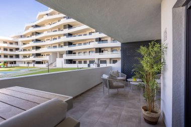 Geniş kaplı balkon, salon mobilyaları, saksı bitkisi ve modern konut kompleksi manzarası.
