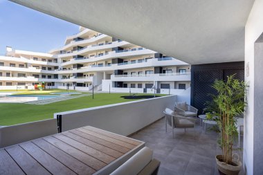 Geniş gölgeli balkon oturma ve yemek alanı, havuza ve çağdaş dairelere bakıyor.