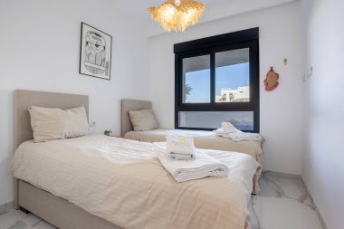 Minimalist ikiz yatak odası, geniş pencereli, hafif yataklı ve katlanmış havluları var.