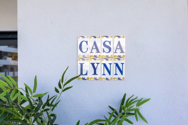 Renkli seramik plaket boyalı kenarı ve yakındaki yeşil yaprakları olan Casa Lynn yazıyor.