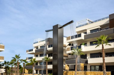 Açık havada duşu ve parlak gökyüzünün altında palmiye ağaçları olan çağdaş apartmanlar.