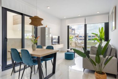 Yemek masası, kapalı kapılar ve balkon manzaralı modern açık yaşam alanı.