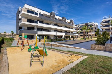 Çocuk parkı, kum sahası, palmiye ağaçları ve asfaltlı açık alanlar olan konut binaları