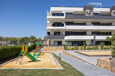 Çocuk parkı, kum sahası, palmiye ağaçları ve asfaltlı açık alanlar olan konut binaları