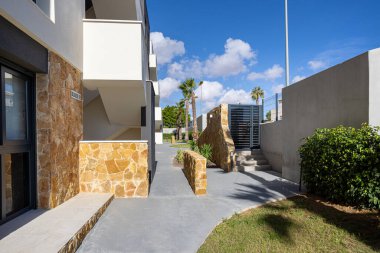 Taş detaylarıyla modern bina cephesi, beton geçit, merdiven, kapı ve palmiye ağaçları