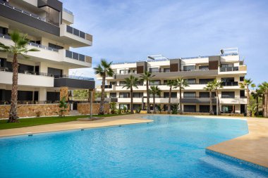 Havuz, palmiye ağaçları ve açık mavi gökyüzü ile güneşli havanın yer aldığı çağdaş konut kompleksi