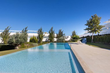 Güneşli bir gün, ağaçlar ve oturma odaları olan manzaralı bir havuz.