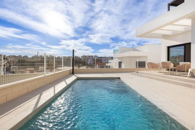 Güneşli terası, minimalist tasarımı ve uzak şehir silueti olan zarif bir özel havuz alanı.