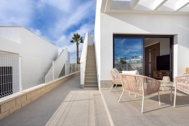 Şık bir teras, örülmüş koltuklar, sürgülü cam kapılar ve çatıya çıkan güneşli merdivenler.