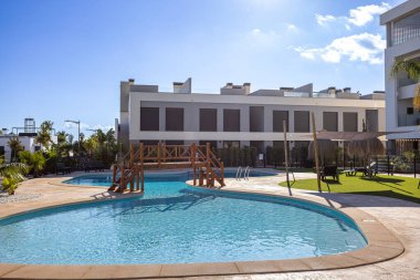 Ahşap köprüsü olan kıvrımlı yüzme havuzu ve çağdaş konut kompleksinde gölgeli dinlenme alanı