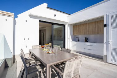 Modern açık hava mutfağı, nötr tonları ve güneşli atmosferi olan şık bir çatı yemek alanı.