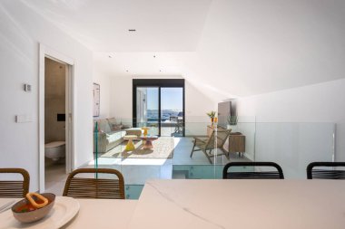 Cam parmaklıkları, deniz manzarası, teras girişi ve modern dekorları olan parlak bir çatı katı.