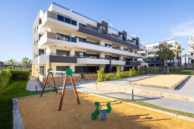 Oyun parkı, peyzaj bahçeleri ve parlak tropikal gün ışığı içeren modern apartman kompleksi.