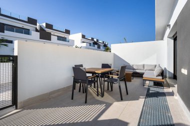 Yemek masası ve kanepesi olan güneşli çağdaş bir avlu.