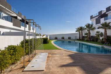 Kavisli bir yüzme havuzunu çevreleyen çağdaş binalar paslanmaz çelik duşlar, palmiye ağaçları ve peyzaj yeşili alanlar..