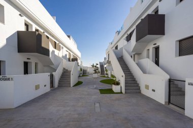 Simetrik dış merdiven, beyaz ve gri cepheler, manzaralı yürüyüş yolları ve parlak mavi gökyüzü altında temiz mimari çizgiler içeren çağdaş yerleşim kompleksi..