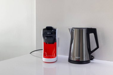 Minimalist mutfak köşesinde kapsül kahve makinesi ve temiz beyaz bir tezgahta paslanmaz çelik su ısıtıcısı var..