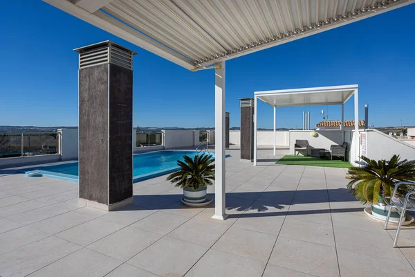 Geniş çatı terası, yüzme havuzu, pergola koltuğu ve mavi gökyüzü, boş zaman, güneşlenme ve mutlu aktif yaşam tarzı için parlak, rahatlatıcı bir atmosfer yaratıyor..