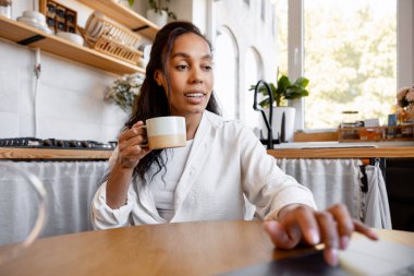 Uzaktan kumandalı bir iş yaşam tarzını somutlaştıran, ev bilgisayarında çalışırken kahveden zevk alan bir kadın.