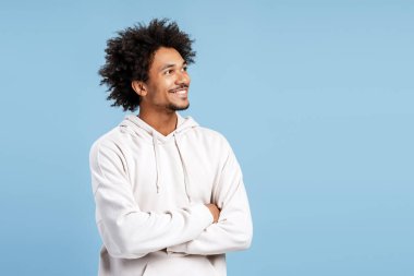 Fotokopi odasına bakan şık kapüşonlu, mutlu, yakışıklı Latin bir adam. Stüdyoda gülümsüyor, mavi arka planda izole halde. Reklam, alışveriş konsepti