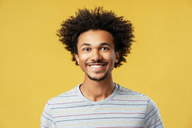 Gülümseyen kıvırcık saçlı, sarı arka planda yalnız poz veren mutlu Afro-Amerikan adam. Reklam, diş bakımı konsepti
