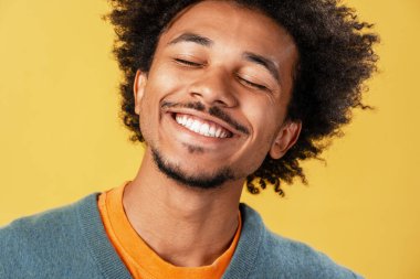 Sarı arka planda izole edilmiş gözleri kapalı gülümseyen, gülümseyen Afrikalı Amerikalı bir adam portresi. Diş sağlığı konsepti