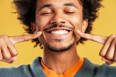 Gülümseyen Afro-Amerikan bir adamın portresi. Sarı arka planda izole edilmiş gözleri kapalı bir şekilde gülümsüyor. Diş sağlığı konsepti