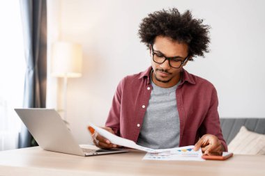 Düşünceli, dalgın, gözlüklü, evdeki oturma odasında dizüstü bilgisayarla çalışan Latin bir adam. Çevrimiçi teknoloji kavramı