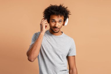 Bej arka planda izole edilmiş kameraya bakan kulaklıkla müzik dinleyen gülümseyen Afrikalı Afrikalı Amerikalı adamın portresi. Çevrimiçi teknoloji kavramı