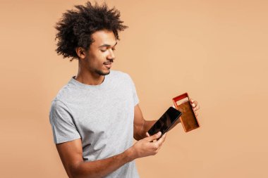 Gülümseyen, Afro-Amerikan bir adam bej arka planda izole edilmiş akıllı telefon için kahverengi telefon kılıfı tutuyor ve gösteriyor. Güvenlik kavramı